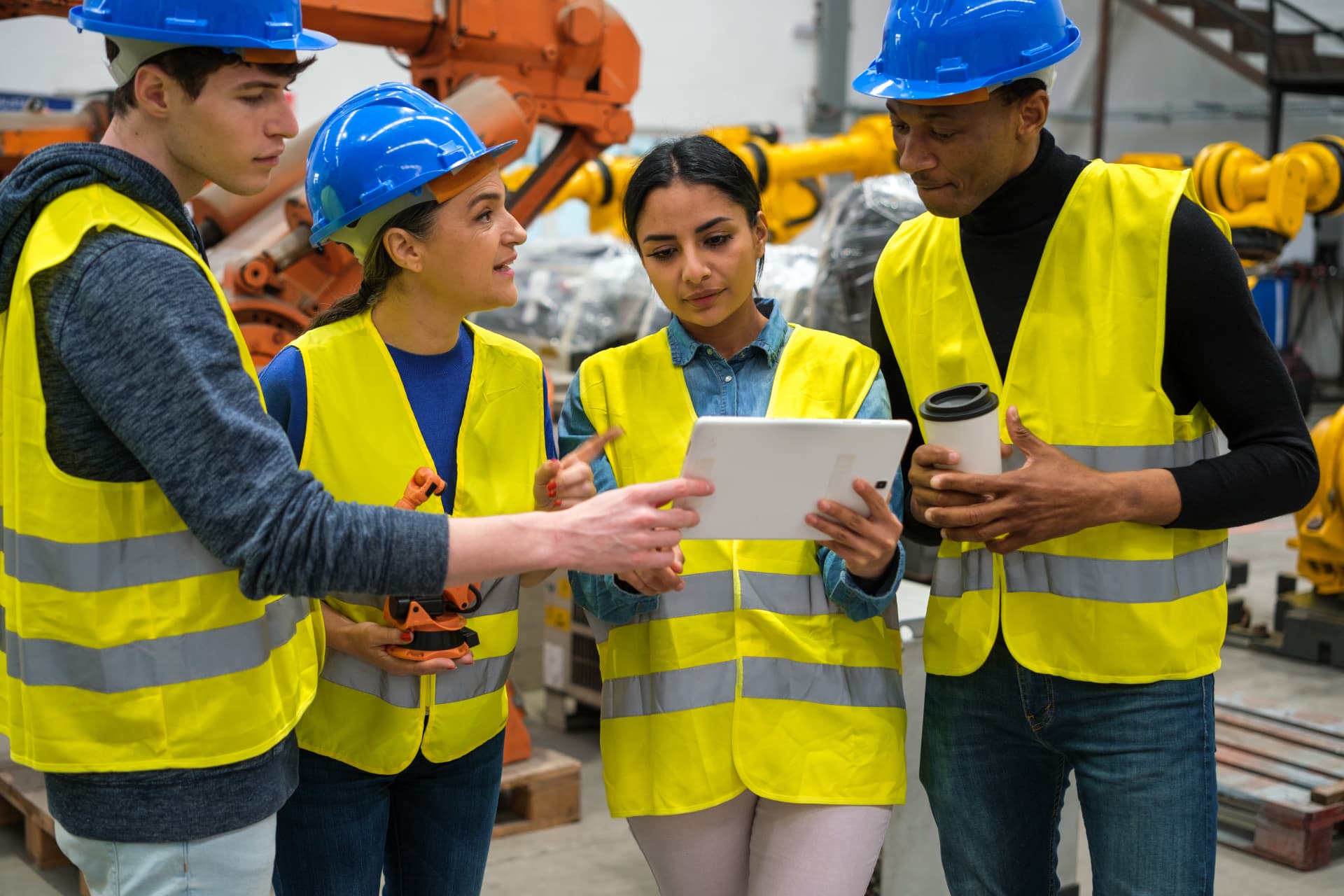 Turning Supervisors Into Leaders, Not Escalators Manufacturing team in hard hats and safety vests reviewing a tablet on the plant floor